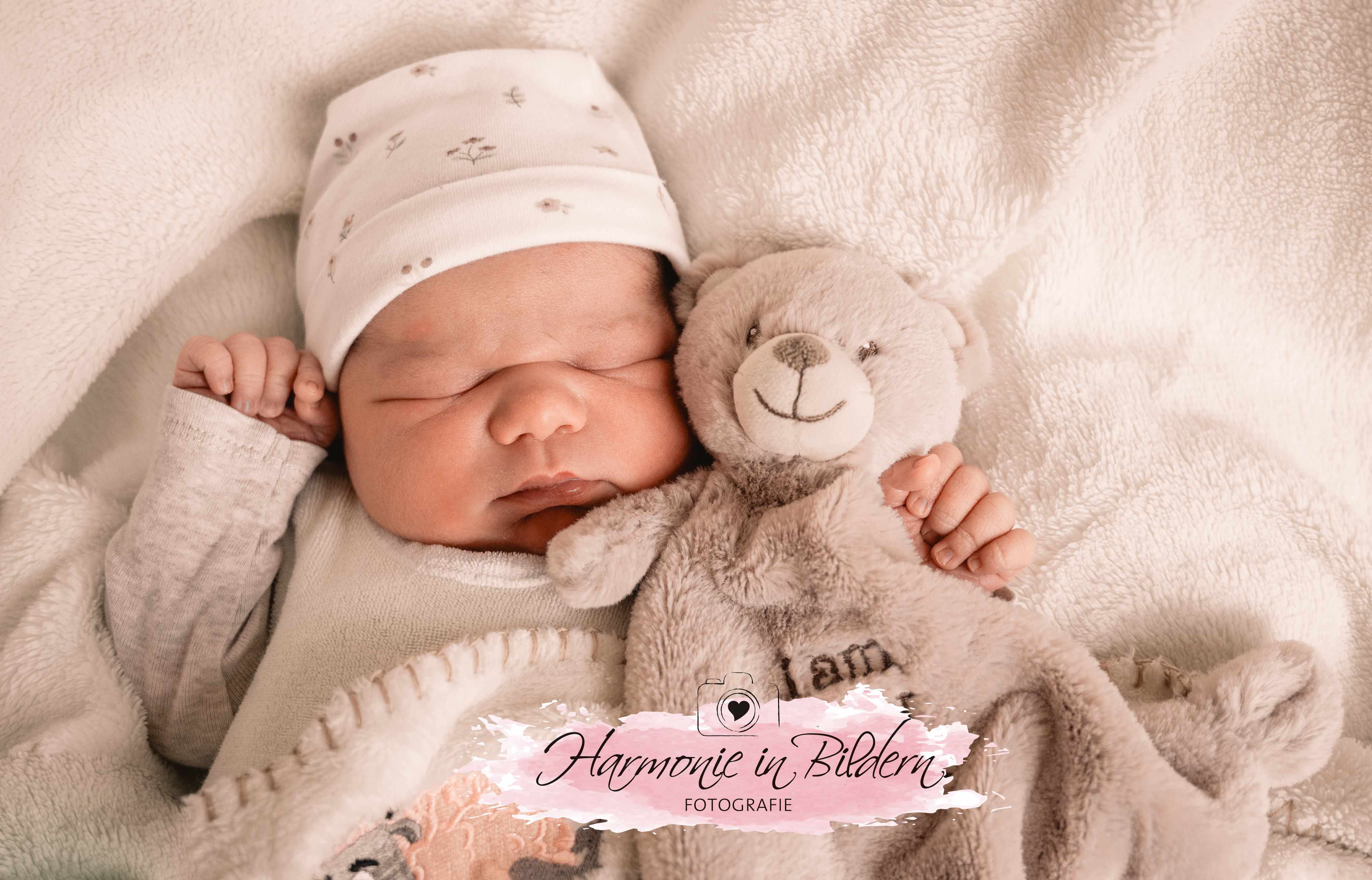 Neugeborenens auf weisser Decke mit Plüschtier im Arm