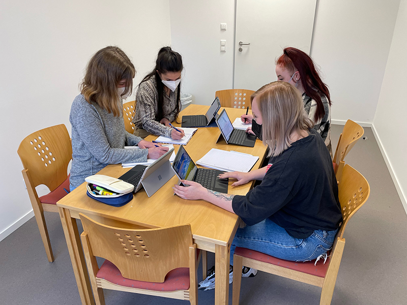 Vier junge Frau sitzen mit Tablets an einem Tisch.