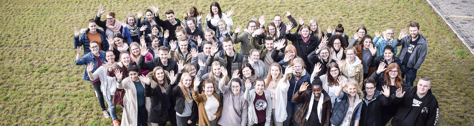 Auszubildende und Studierende stehen auf einer Wiese und winken
