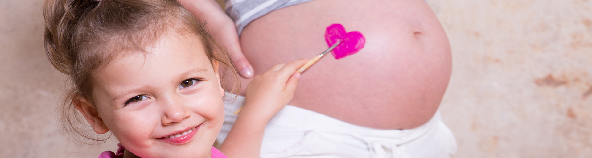 Ein kleines Mädchen mal ein Herz auf den schwangeren Bauch der Mutter.
